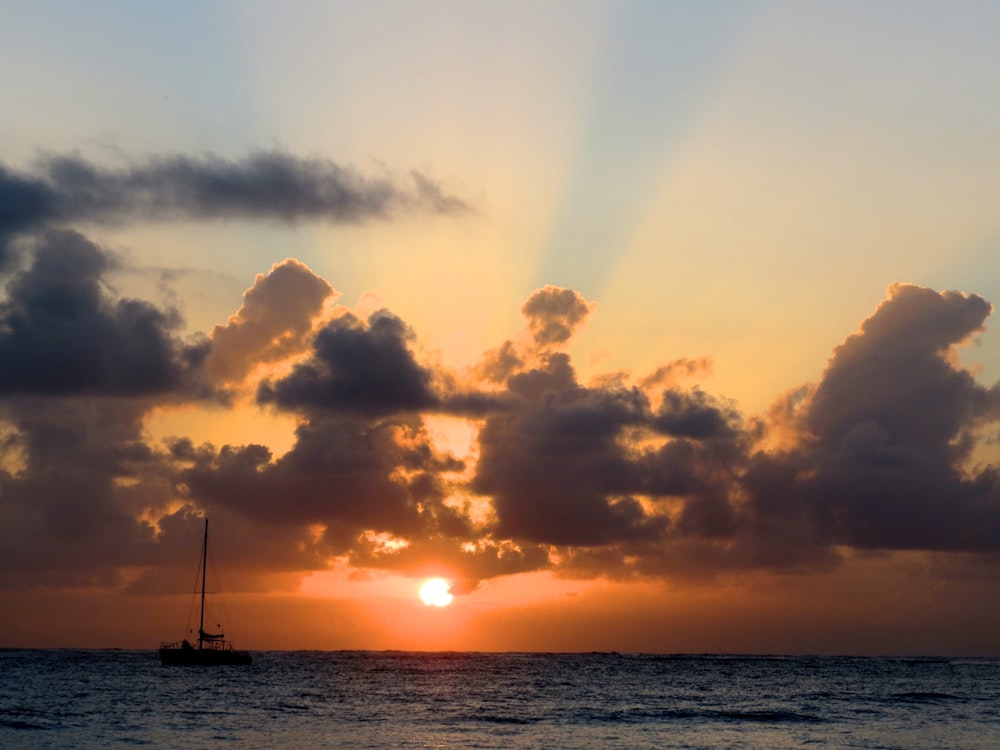 the sun is setting over the ocean with a sailboat in the foreground