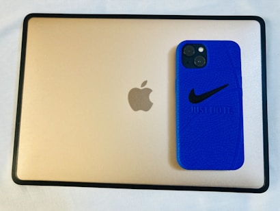 A blue smartphone case with a Nike logo and the phrase 'Just Do It' sits on top of a gold-colored tablet with an Apple logo.