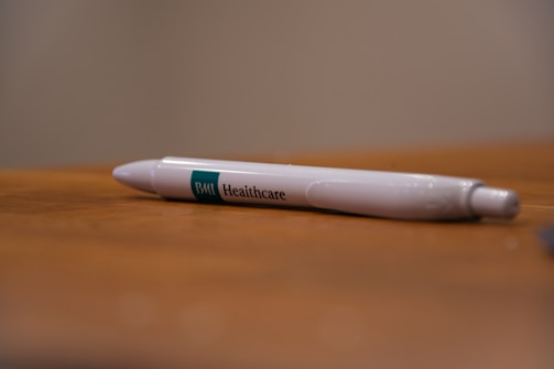 A white pen with 'BMI Healthcare' printed on it rests on a wooden surface. The background is blurred, highlighting the pen as the focal point.