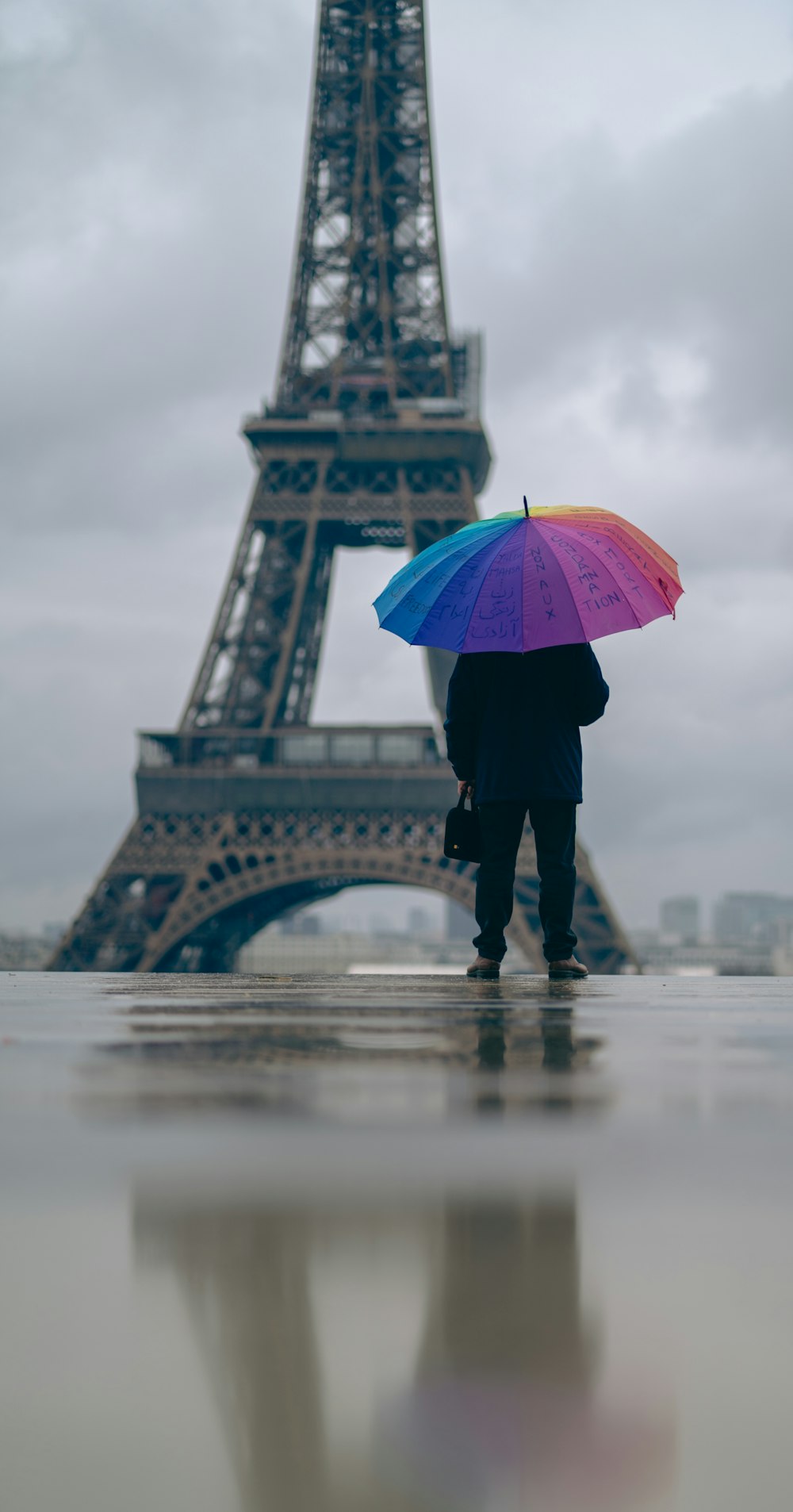 Una persona sosteniendo un paraguas frente a la Torre Eiffel