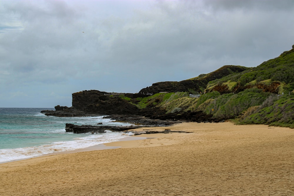 a sandy beach next to the ocean under a cloudy sky