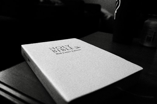 Monochrome image of an open Bible with hands resting gently on the pages.