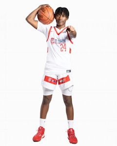 A basketball player wearing a white and red uniform holds a basketball above their head with one hand while pointing forward with the other. The uniform displays the number 24 and the word 'C Town'. The player is wearing red sneakers and standing on a plain white background.