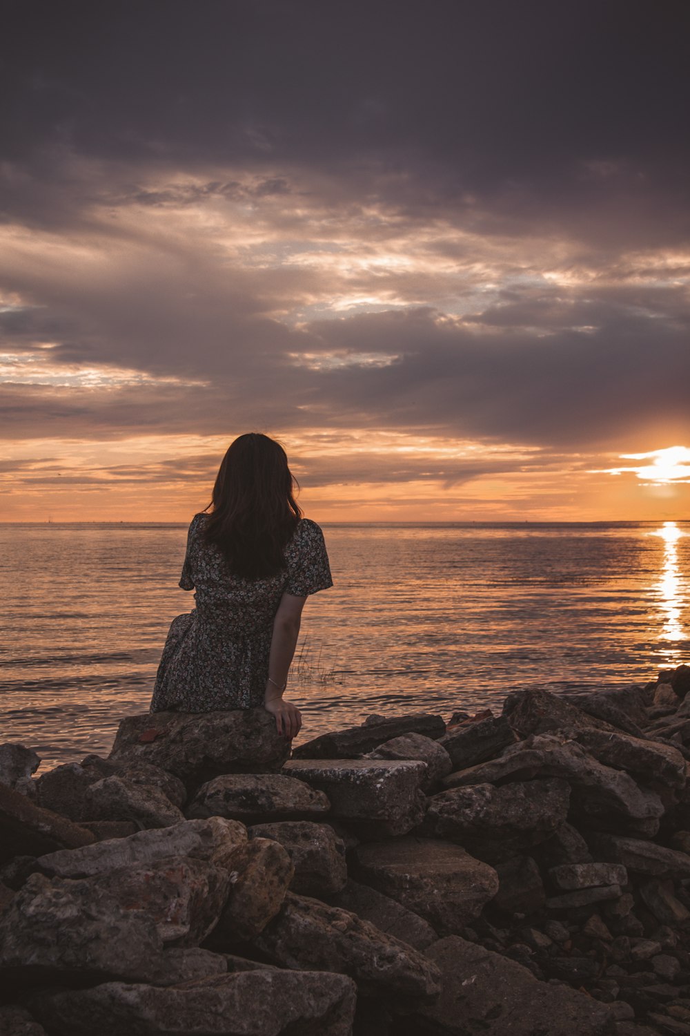 a woman sitting on rocks looking out at the ocean