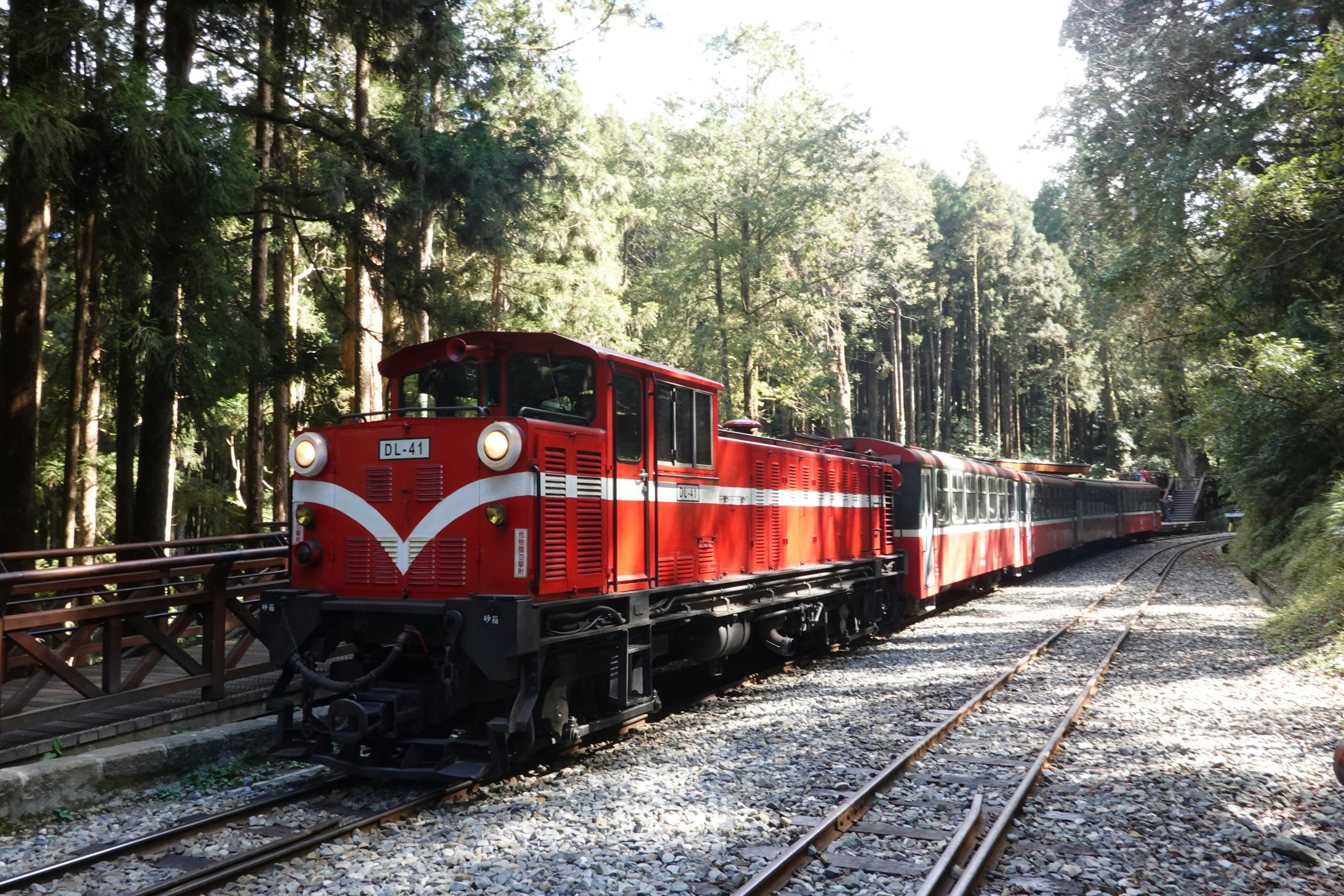 a red train traveling down train tracks next to a forest