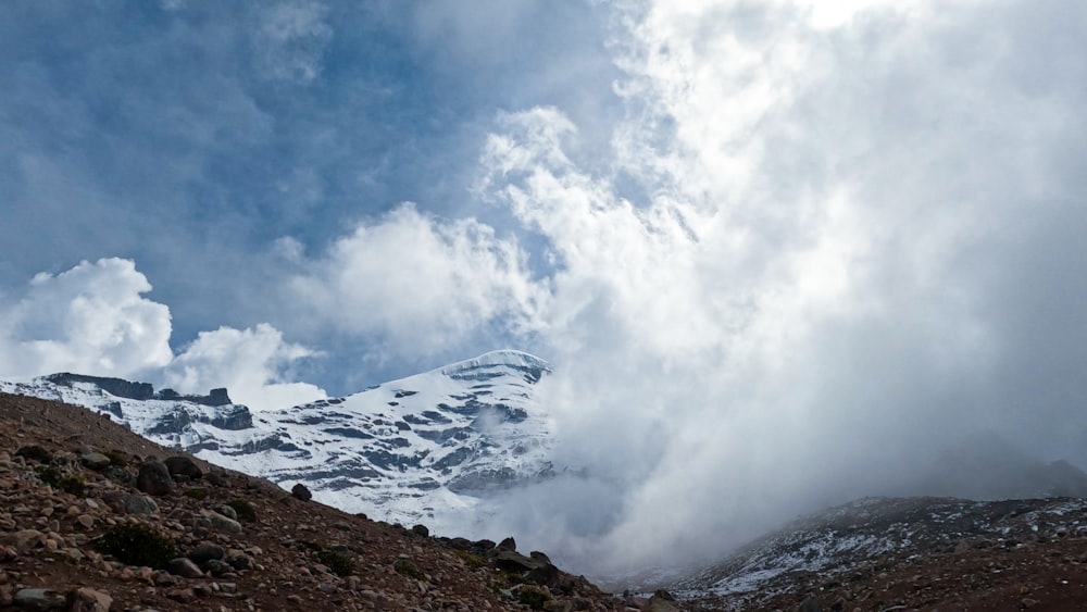 a mountain covered in snow and clouds under a blue sky