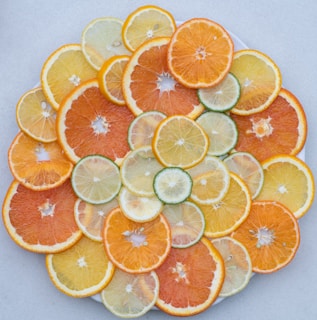 A neatly arranged assortment of citrus fruit slices, including oranges, lemons, and limes. The slices are overlapped in a circular pattern, showcasing a variety of textures and vibrant colors on a light background.