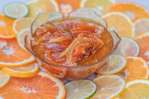 Close-up of a jar of vibrant orange marmalade with fresh citrus slices beside it