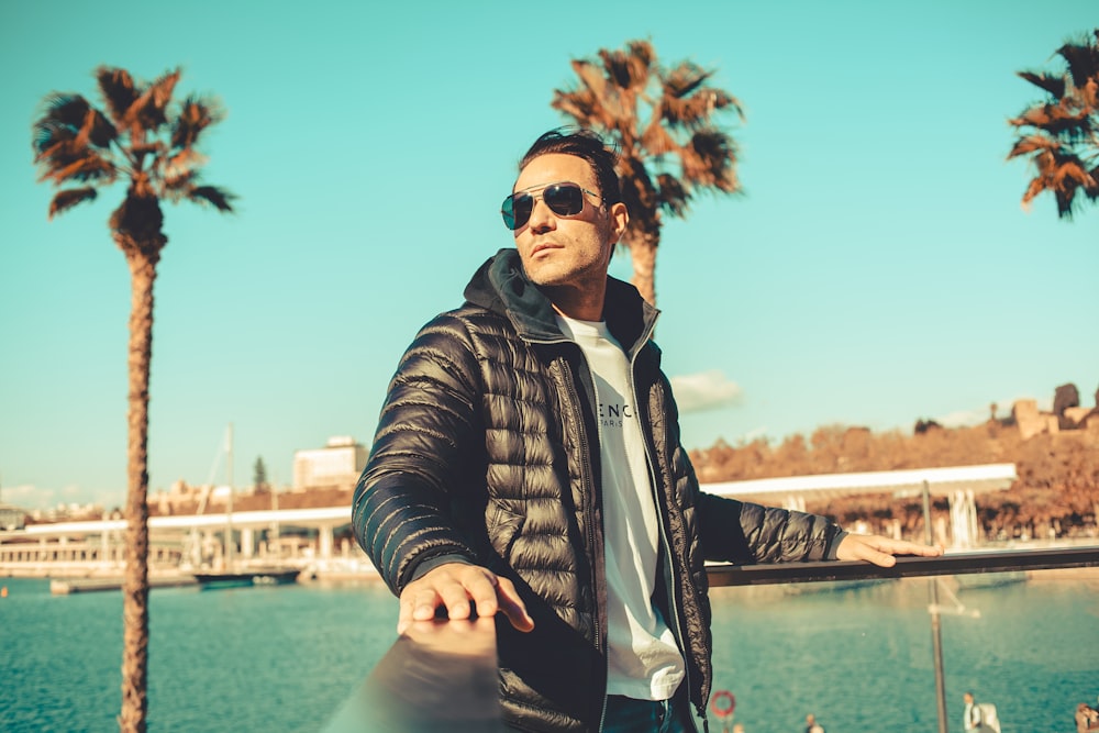 a man in a black jacket and sunglasses leaning on a rail