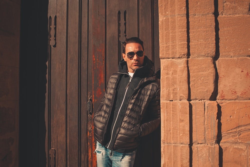 a man wearing sunglasses leaning against a brick wall