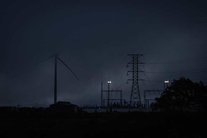 Power transmission towers and wind turbine at night under storm clouds