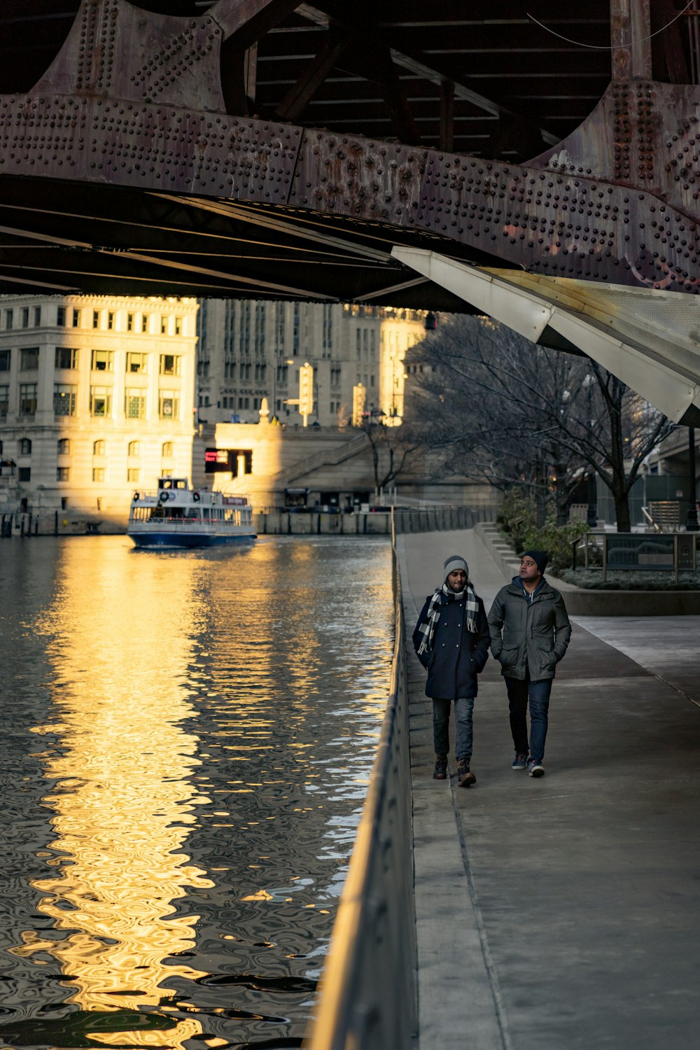 a couple of people walking down a sidewalk next to a body of water