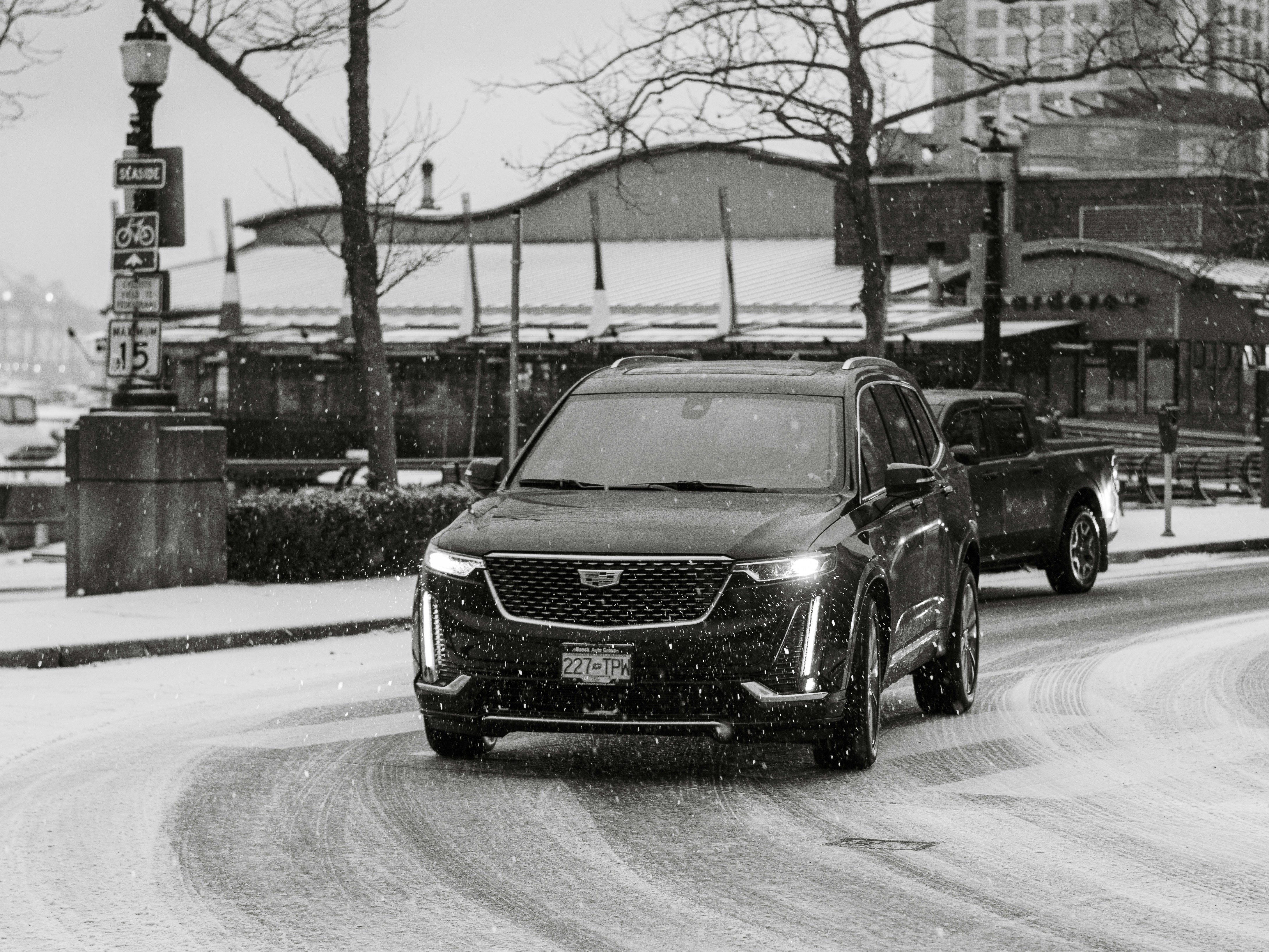 A black and white photo of a car driving down a snowy street photo ...
