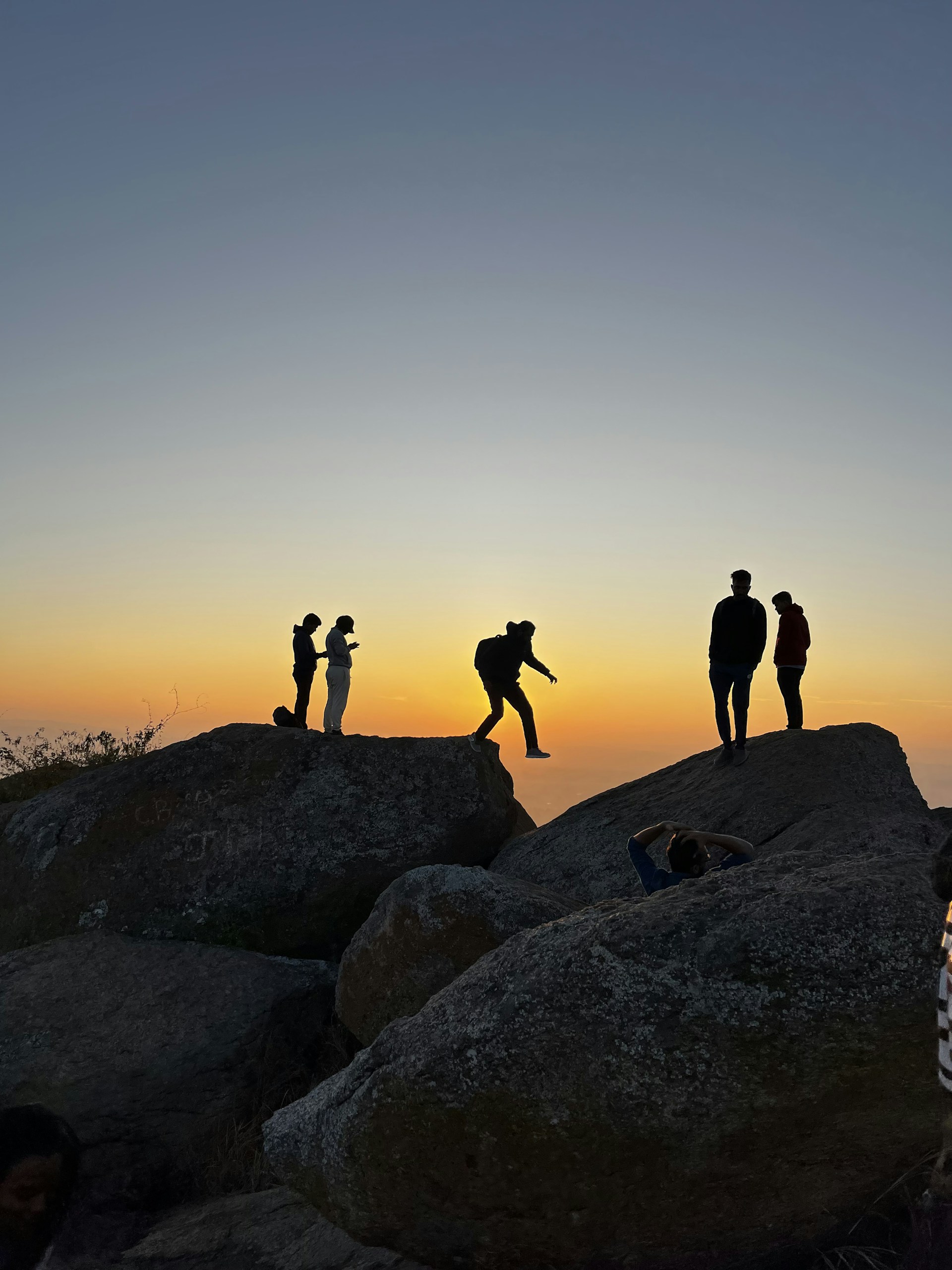 A group of friends enjoying a bouldering session at a scenic outdoor location during sunset.