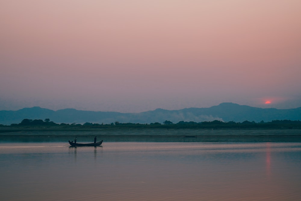 a boat floating on top of a lake at sunset