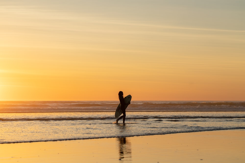 una persona che tiene una tavola da surf che cammina sulla spiaggia