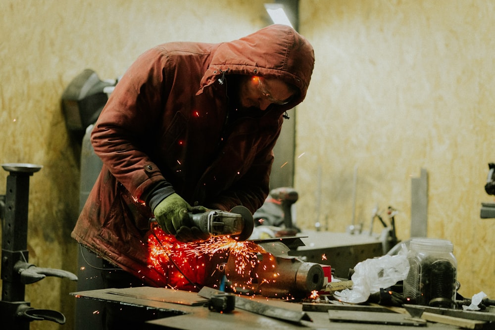 a man in a red jacket working on a piece of metal