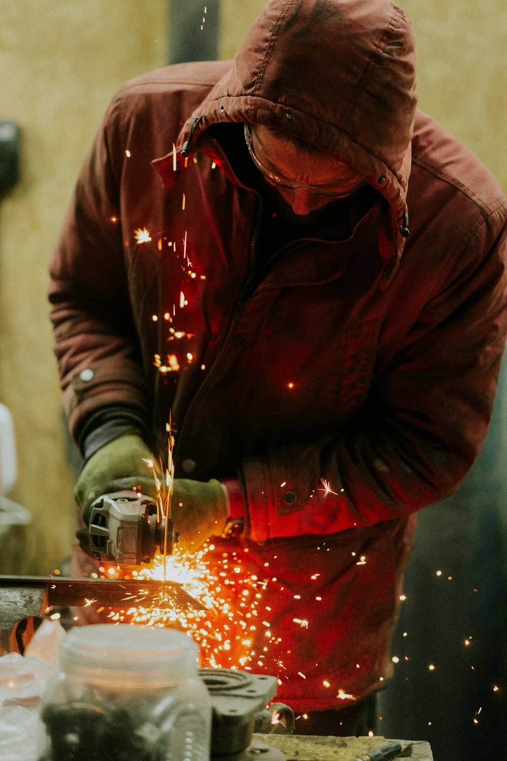 a man in a red jacket grinding metal with a grinder