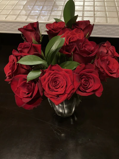 A vibrant bouquet of deep red roses with lush green leaves, freshly arranged in a clear glass vase.