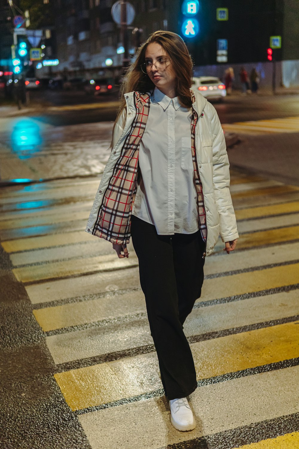 a woman walking across a cross walk at night