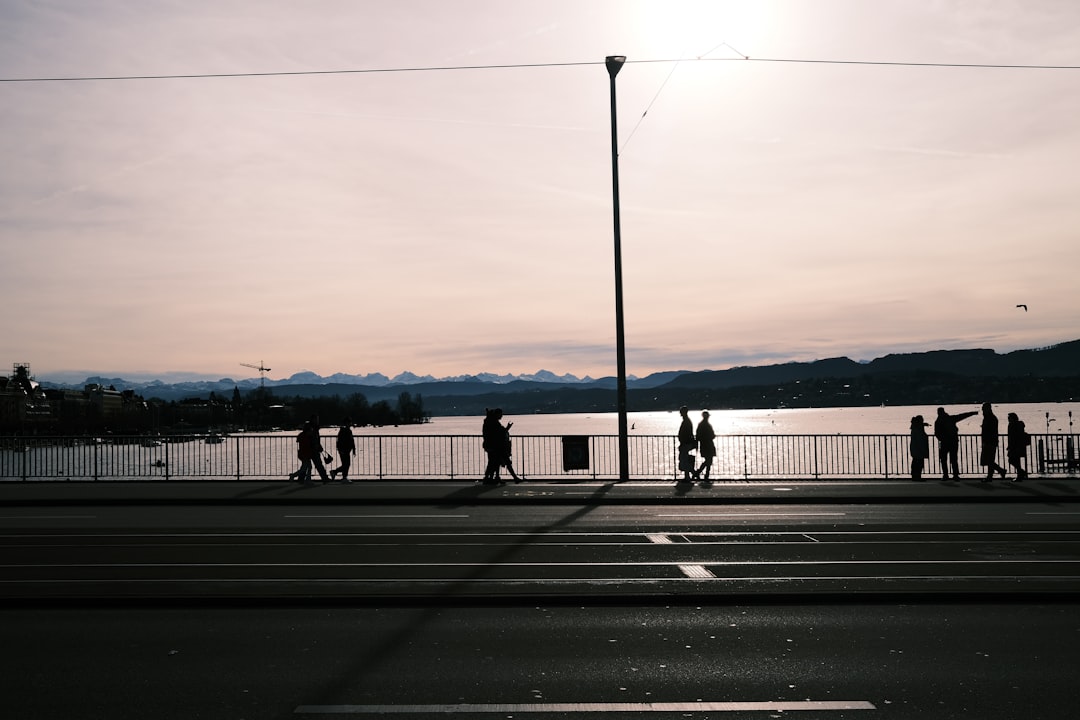 a group of people walking across a street next to a body of water