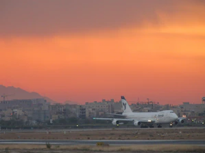 Modern commercial airplane taxiing on runway at sunset.