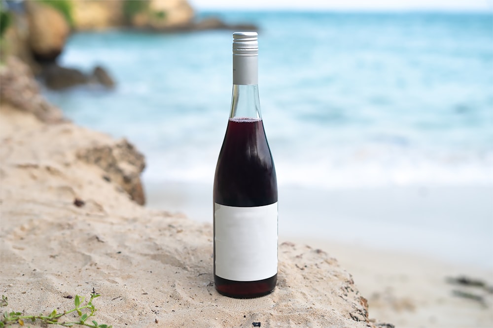 a bottle of wine sitting on top of a sandy beach