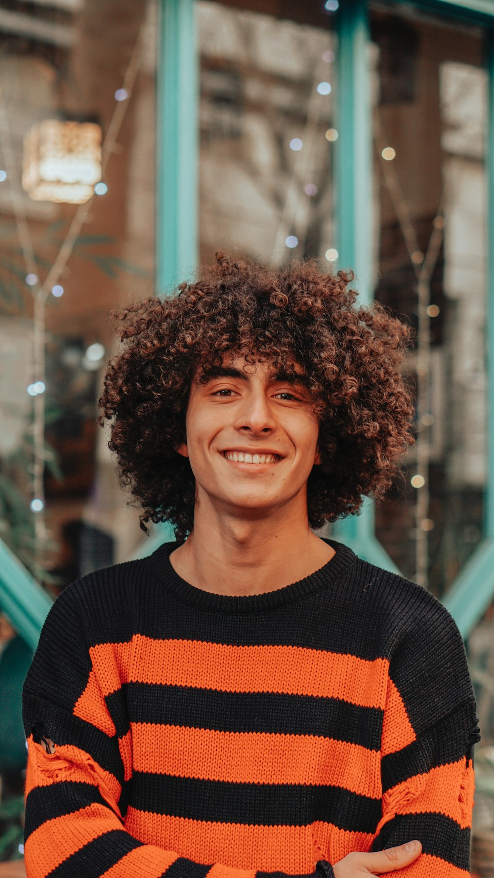a man with curly hair wearing an orange and black striped sweater