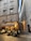 An outdoor restaurant setting with people dining at tables under a canopy labeled 'Osteria Del Gallo.' The scene is situated in a narrow, cobblestone alleyway between tall, old buildings with shuttered windows. Warm lighting creates a cozy and inviting atmosphere.