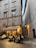 An outdoor restaurant setting with people dining at tables under a canopy labeled 'Osteria Del Gallo.' The scene is situated in a narrow, cobblestone alleyway between tall, old buildings with shuttered windows. Warm lighting creates a cozy and inviting atmosphere.