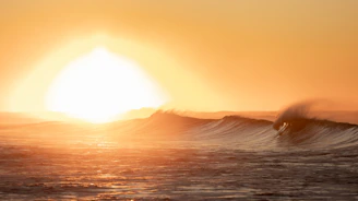 A serene ocean scene at sunrise with gentle waves glowing golden under a bright yellow sun.