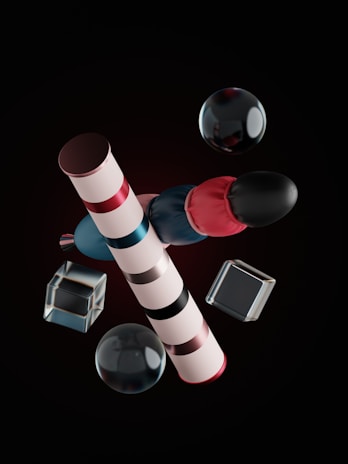 The image features geometrically arranged objects including striped cylindrical shapes, spheres, and transparent cubes. The objects are presented against a dark background and exhibit reflections and highlights, suggesting a glossy or metallic texture.