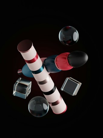 The image features geometrically arranged objects including striped cylindrical shapes, spheres, and transparent cubes. The objects are presented against a dark background and exhibit reflections and highlights, suggesting a glossy or metallic texture.
