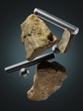 Floating rocks and metallic elements are arranged in a surreal, gravity-defying composition against a dark background. The rocks have a rough texture and vary in size, while the metallic elements include smooth cylinders and a shiny sphere.
