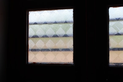 Two textured glass windows with geometric patterns comprised of intersecting diagonal lines and horizontal blue stripes. The background light subtly changes between different shades of blue and beige.