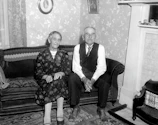 Elderly couple sharing a quiet moment in a sunlit living room with subtle tech devices in the background.