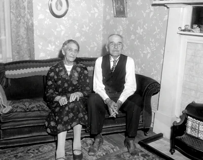 Elderly couple sharing a quiet moment in a sunlit living room with subtle tech devices in the background.
