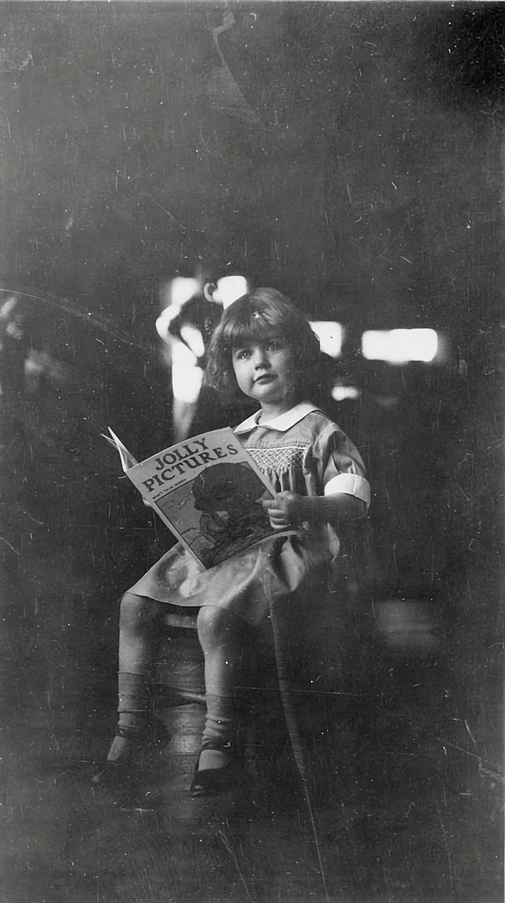 a little girl sitting on a chair reading a newspaper