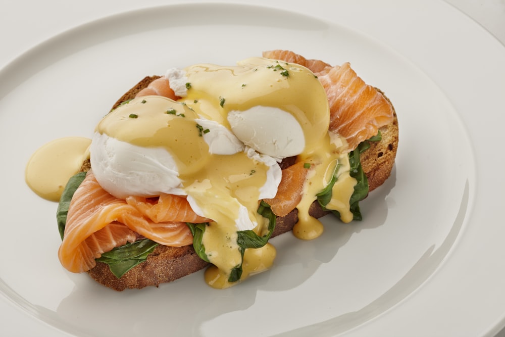 a white plate topped with a sandwich covered in eggs and salmon