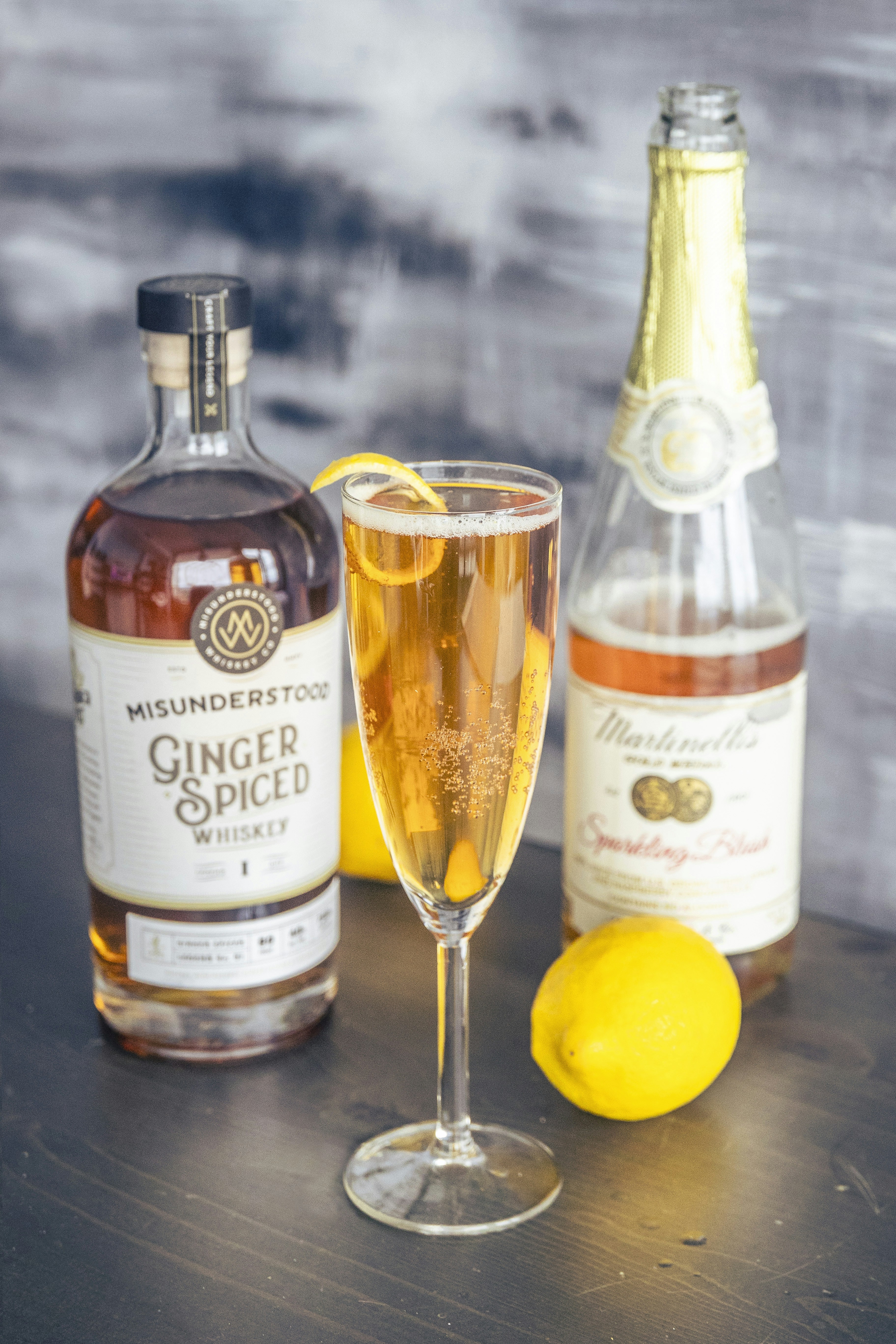 a bottle of ginger spiced whiskey and sparkling wine with a sparkling cocktail garnished with lemon twist