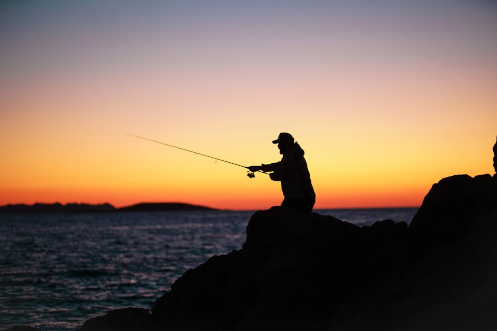 a man standing on a rock fishing at sunset