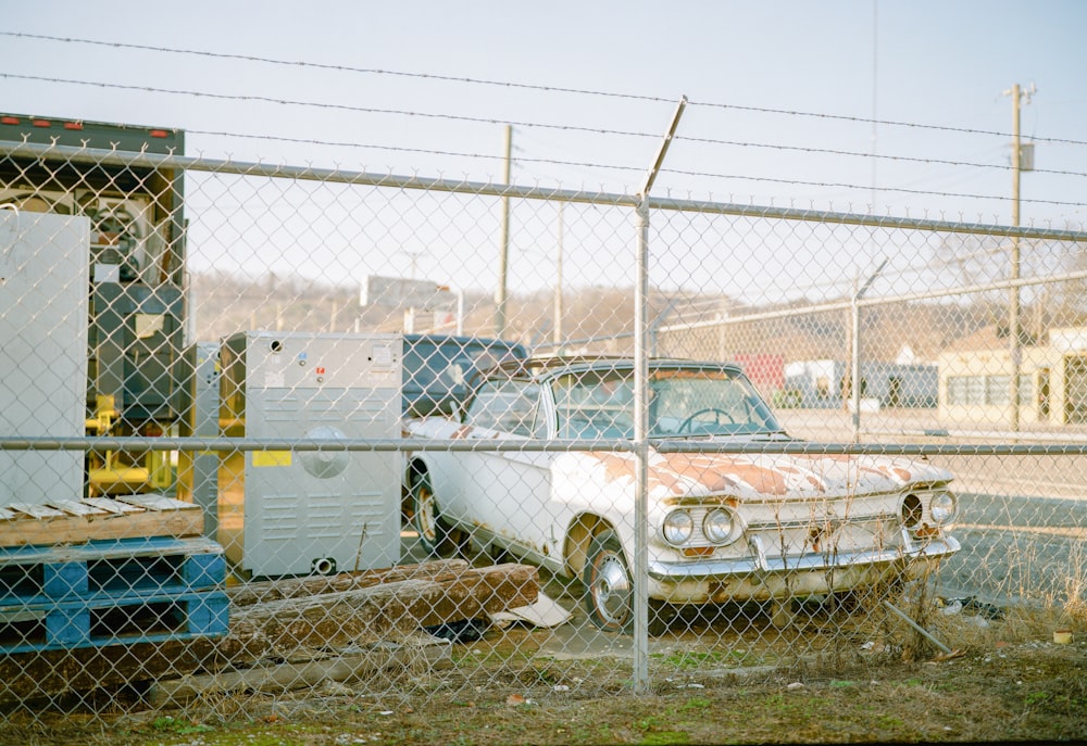 an old car is parked behind a chain link fence