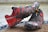 A pair of muddy red and black trail running shoes with prominent logo and design elements are placed on a doormat. The shoes are heavily soiled, suggesting they were used in a rugged outdoor environment. The background shows a neutral, blurred surface.