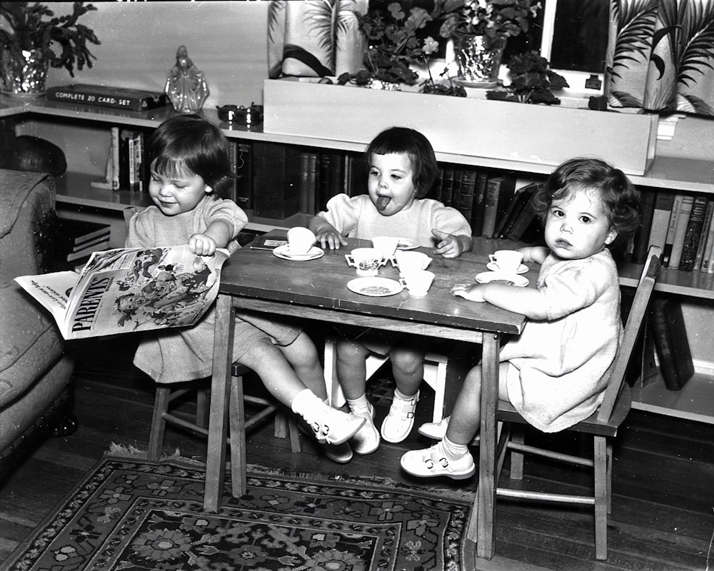 a black and white photo of three children sitting at a table