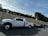 A large white pickup truck is parked on a street, attached to a flatbed trailer. The area is residential, with a high beige wall and green hedges along the sidewalk. Power lines run overhead, and there is a no parking sign nearby.