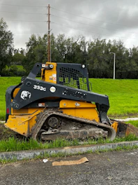 A rugged skid steer loader working on a freshly paved road under a cloudy sky.