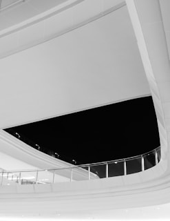 The image features a modern architectural design with curved lines and clean surfaces. A large black void contrasts with the sleek, reflective materials of the structure. Glass railings and subtle lighting details contribute to the minimalist aesthetic.
