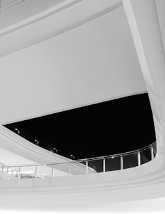 The image features a modern architectural design with curved lines and clean surfaces. A large black void contrasts with the sleek, reflective materials of the structure. Glass railings and subtle lighting details contribute to the minimalist aesthetic.