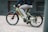 A person is riding a light green electric bicycle with the brand name 'Levit' visible on the frame. The cyclist is dressed casually in a dark top and light gray pants, moving swiftly on a paved surface. The background is slightly blurred, suggesting motion.