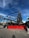 Several large construction lifts are parked in an outdoor lot, each with long extendable arms. Bright red barricades are placed in front of the machinery. The sky above is a clear, vivid blue with some wispy clouds.